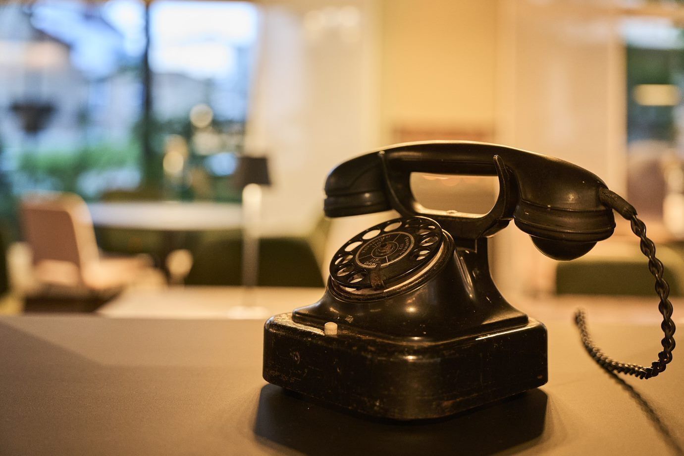 A vintage black telephone on a table in a room with a blurred background.