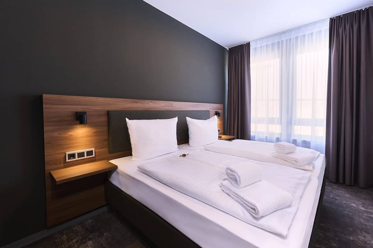 A modern hotel room with a large bed, dark walls, and a window with curtains.