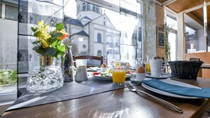 Une table dressée pour le petit-déjeuner, avec un vase de fleurs, une carafe, un verre de jus d’orange et une assiette contenant des œufs et des toasts.