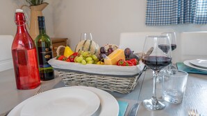 A dining table with a fruit basket, wine bottles, and glasses. - Rosemary Cottage - Three Bedroom House, Sleeps 5 (Mortehoe)