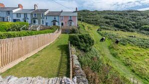 A residential area with a stone wall, a wooden fence, and a grassy hill with sheep. - Rosemary Cottage - Three Bedroom House, Sleeps 5 (Mortehoe)