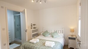 A bedroom with a bed, a bedside table, a nightstand, a lamp, and a bathroom with a shower. - Seashells - Three Bedroom House, Sleeps 6 (Woolacombe)