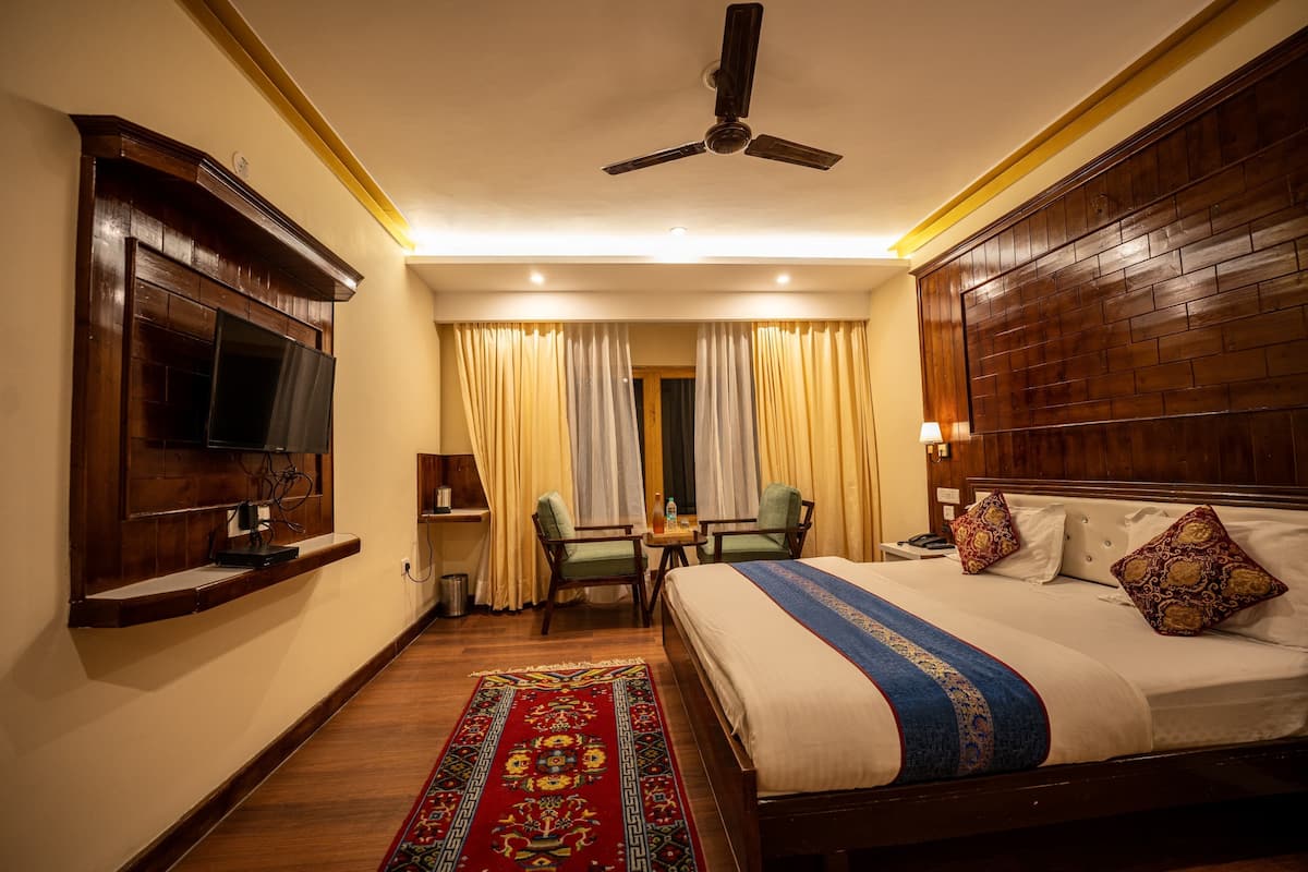 A hotel room with a bed, a desk with a chair, a television on the wall, and a ceiling fan.