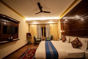A hotel room with a bed, a ceiling fan, a TV, a desk, and a chair. - The Hunder Eco Villa (Leh)