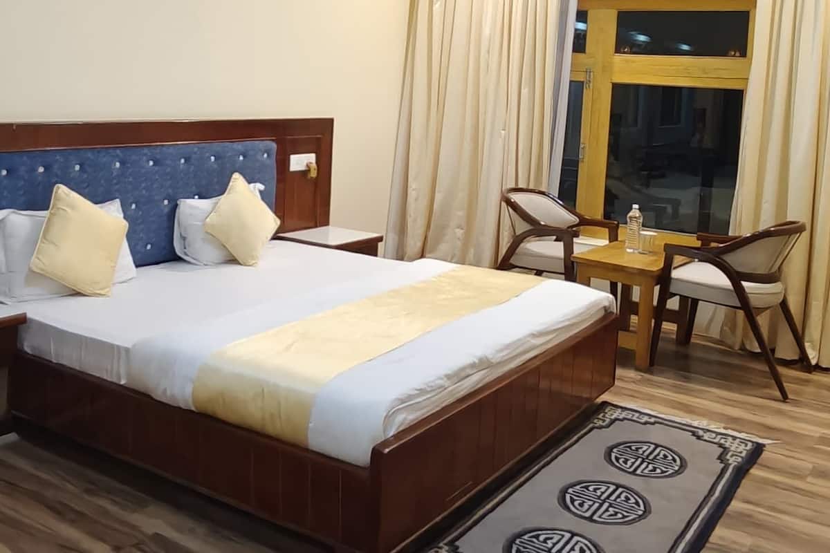 A hotel room with a bed, a ceiling fan, a small table with chairs, and a window with curtains.