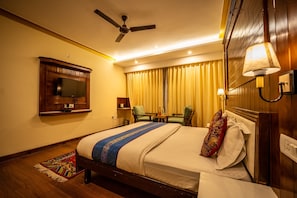 A hotel room with a bed, a television mounted on the wall, a ceiling fan, a table with chairs, and a lamp. - The Hunder Eco Villa (Leh)