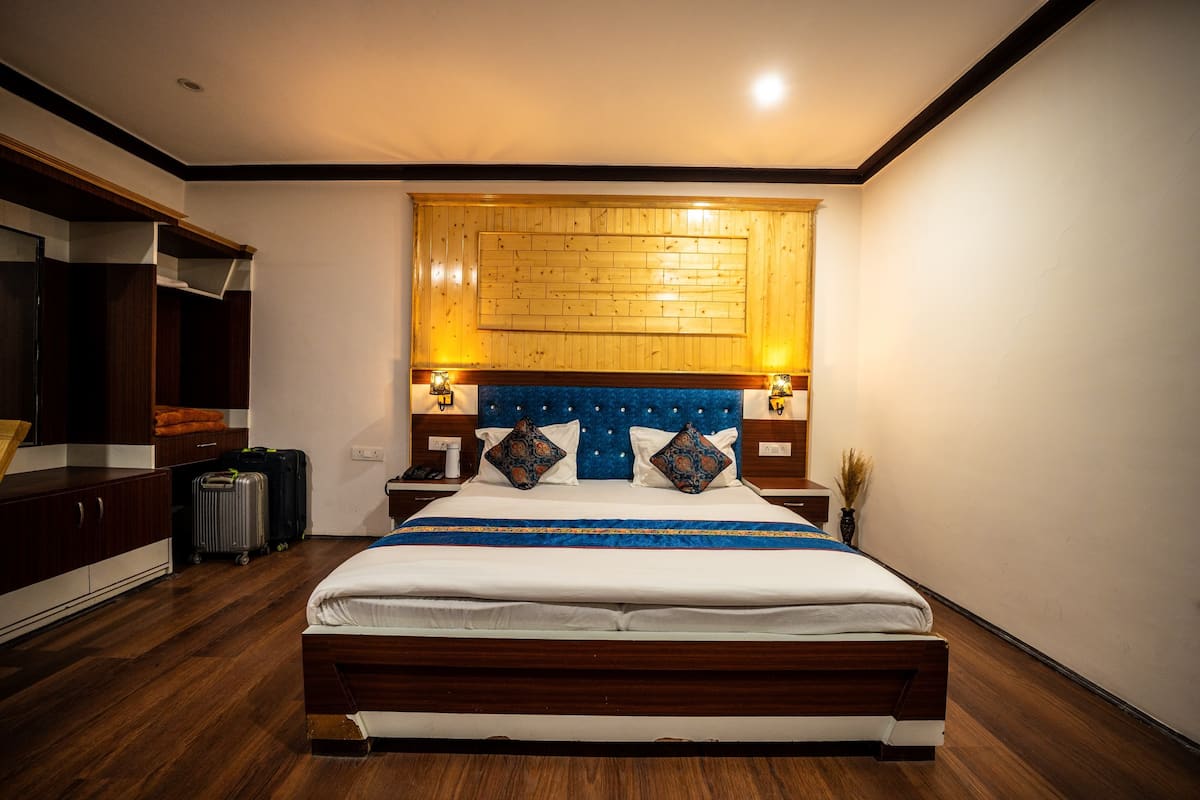 A hotel room with a wooden headboard, a large bed, a wardrobe, and a suitcase on the floor.