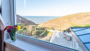 Vista desde una ventana con un paisaje costero, un patio y una mesa con sillas.