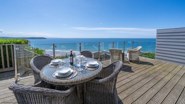 A dining area with a table set for four, overlooking a beach and the sea.