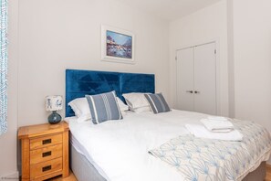 A bedroom with a large bed, a wooden nightstand, a framed painting, and a white door.