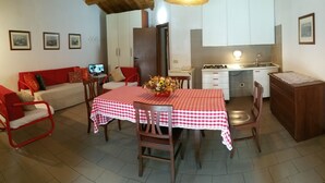 Un'area pranzo con tovaglia a scacchi rossi e bianchi, sedie di legno e un vaso di fiori. Si nota una sedia rossa e un divano con cuscini sullo sfondo.