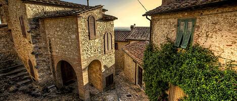 A narrow cobblestone street with stone buildings, arched doorways, and green shutters.