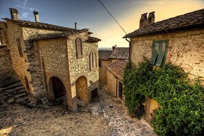 A narrow cobblestone street with stone buildings, arched doorways, and green shutters. - Apartment in a country house on a hill with a view of the sea, a large park, and a pool (Casale Marittimo)