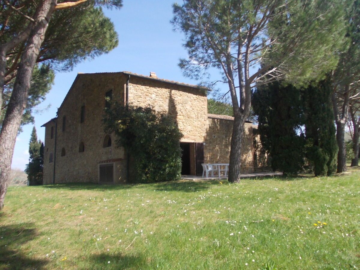A stone building with a large open doorway, surrounded by trees and a grassy area.