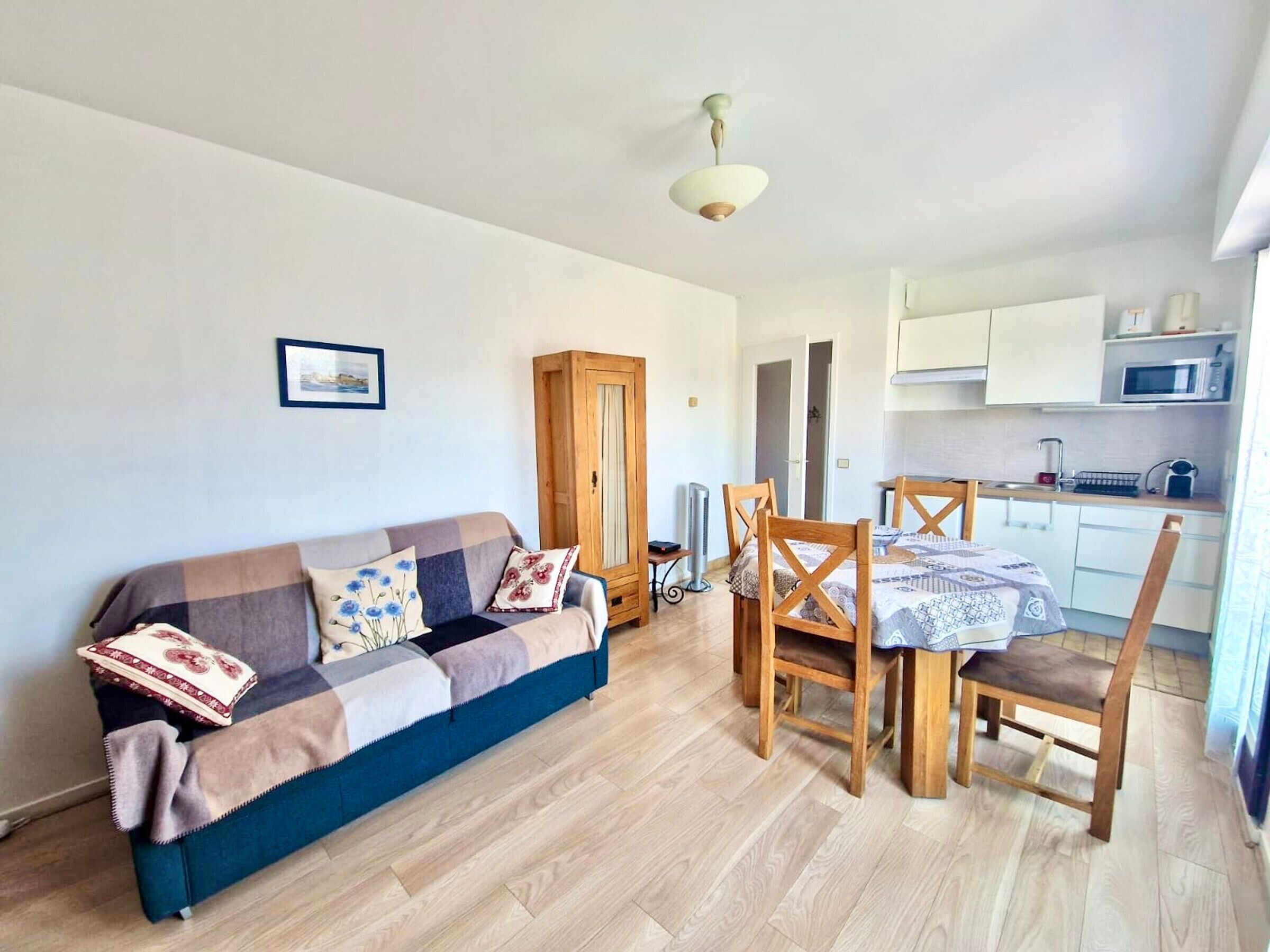A cozy living room with a sofa, wooden chairs, a dining table, and a kitchen area with cabinets and a microwave.