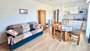A cozy living room with a sofa, wooden chairs, a dining table, and a kitchen area with cabinets and a microwave. - Cozy Apartment Downtown Annecy, Parking, Wi-Fi Included (Annecy)