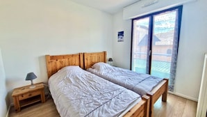 A bedroom with two wooden beds, a small bedside table with a lamp, and a large window with a view of a building. - Cozy Apartment Downtown Annecy, Parking, Wi-Fi Included (Annecy)