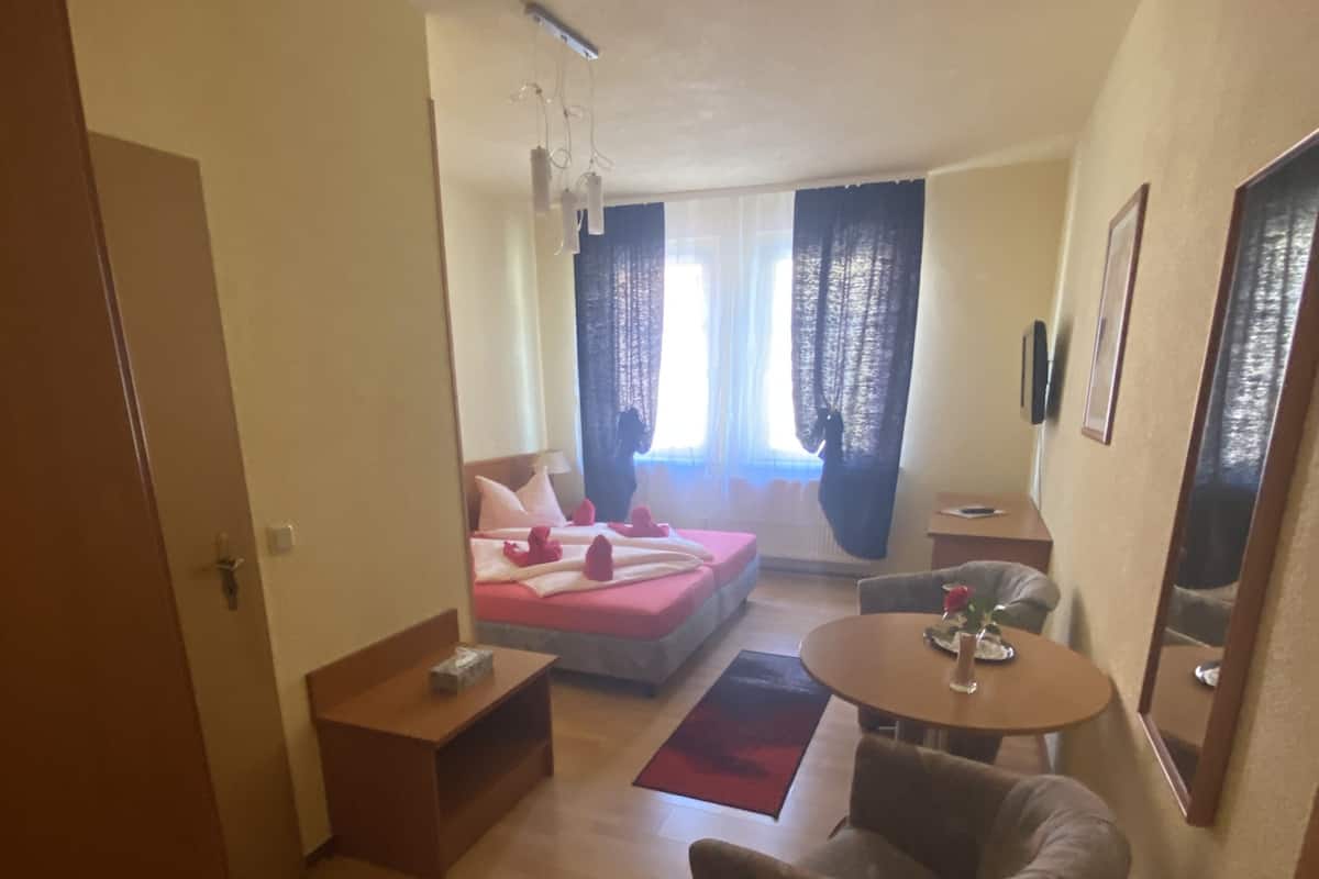 A compact hotel room with a bed, a small table, a chair, and a window with curtains.
