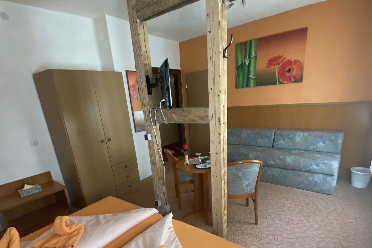 A hotel room with a bunk bed, a wooden ladder, a desk with a chair, a sofa, and a television mounted on the wall.