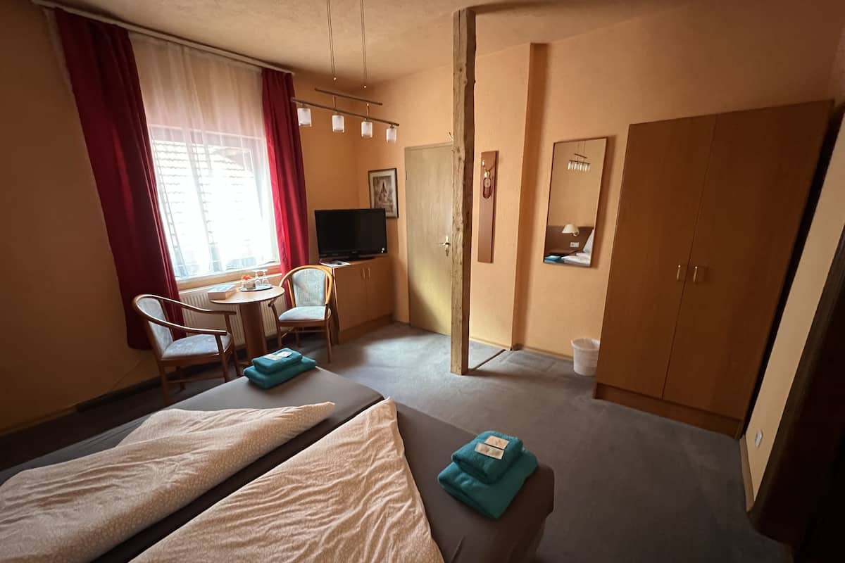 A hotel room with two beds, a desk, a chair, a television, and a wardrobe.