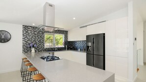 Une cuisine moderne dotée d’un îlot central, de tabourets de bar, d’un réfrigérateur en acier inoxydable et d’une fenêtre donnant sur un espace verdoyant.
