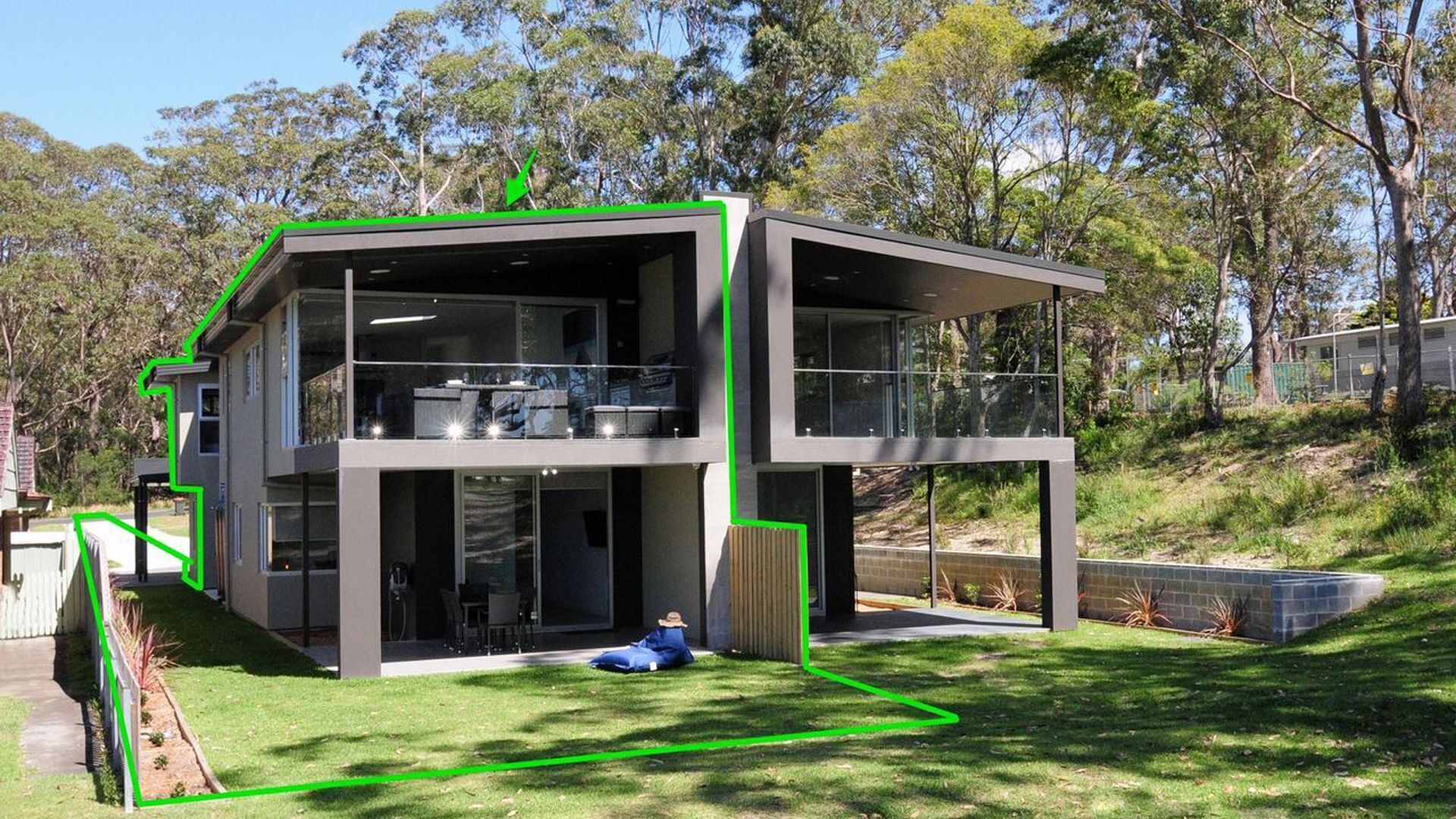 A modern two-story house with a flat roof, large windows, and a balcony.