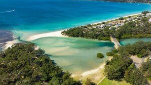 Vue aérienne d’une zone côtière avec une plage, des eaux cristallines et un quartier résidentiel avec des maisons.