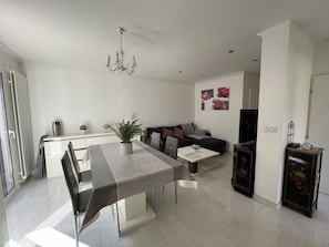 Una sala de estar moderna con comedor, que incluye una araña, un sofá, una mesa de centro y un mueble para televisión.