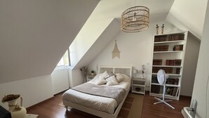Ein Schlafzimmer mit schrägen Wänden, einem Bett, einem Nachttisch, einer Stehlampe, einem Bücherregal und einer Heizung.