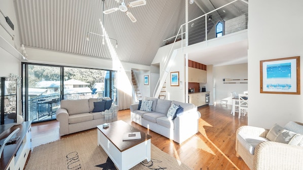 A spacious living area with a large sliding glass door leading to a balcony, a sofa, a coffee table, and a kitchen area with a dining table.