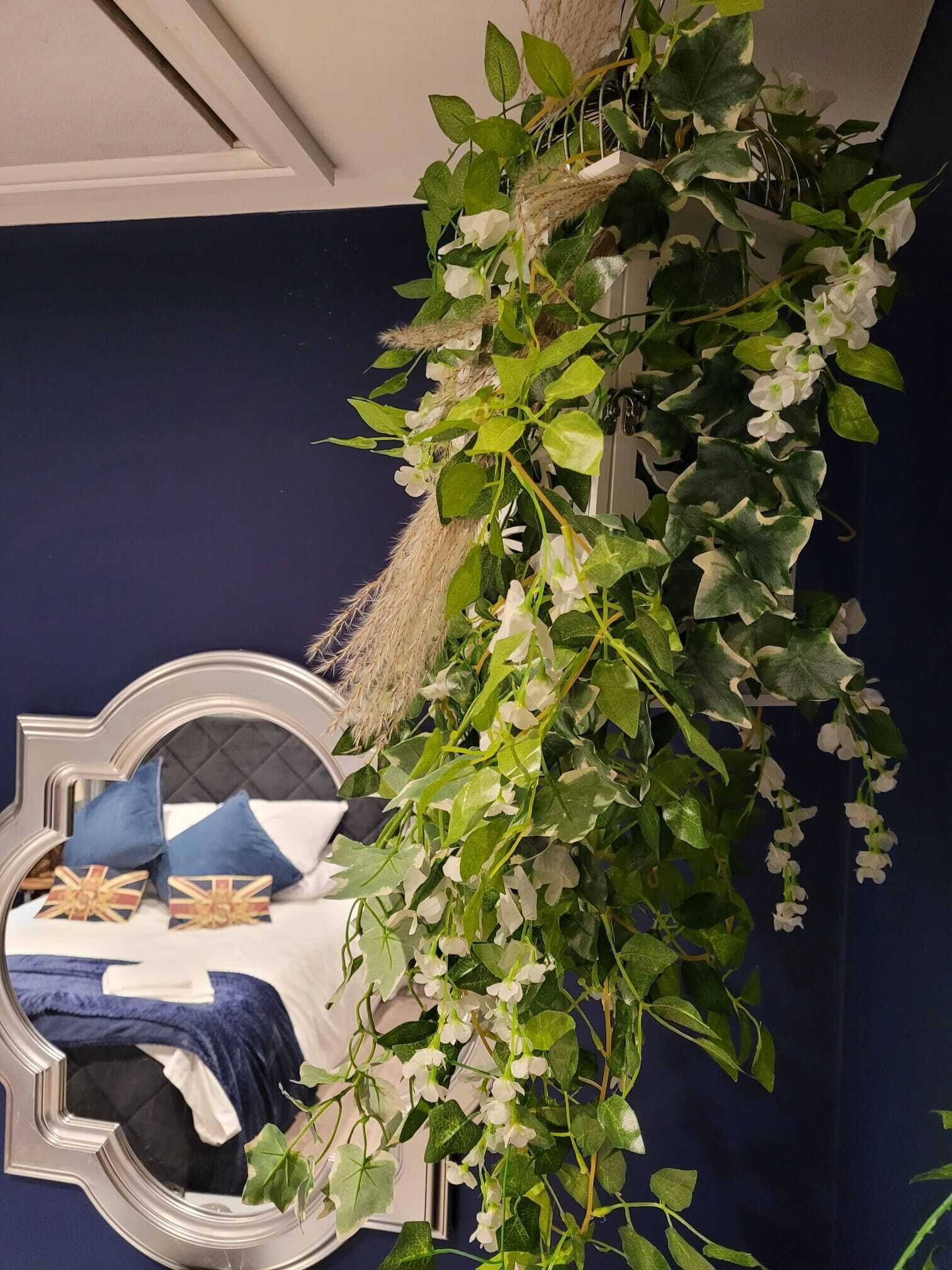 Una habitación con un espejo grande, una cama con ropa de cama azul y un arreglo decorativo de plantas.