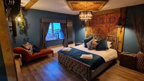 Un dormitorio con una cama grande, un sofá rojo, una ventana con cortinas y un panel decorativo en la pared.