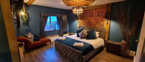 A bedroom with a large bed, a red sofa, a window with curtains, and a decorative wall panel.