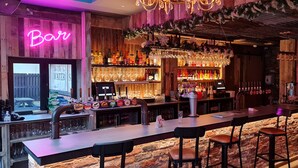 Un bar con un letrero de neón, paredes de madera y una variedad de botellas y vasos.