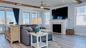 A spacious living room with a fireplace, a television, and a ceiling fan. - Brand New Construction with a Private Pool, Water Views, & Parking for Four! (Cape May)