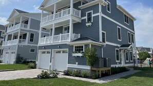 A multi-story residential building with a balcony, a garage, and a small garden area. - Brand New Construction with a Private Pool, Water Views, & Parking for Four! (Cape May)