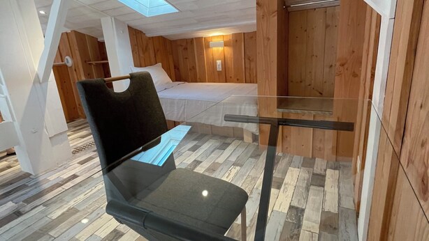 Una habitación moderna con una mesa de vidrio, suelo de madera y techo inclinado con tragaluces.