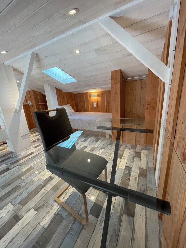 Een moderne kamer met een glazen tafel, houten vloer en een schuin plafond met dakramen.