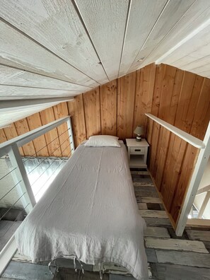 Een eenpersoonsbed in een kamer met houten wanden en een schuine plafond.