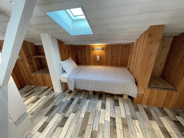 A room with a skylight, wooden walls, a bed, and a small seating area.