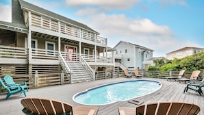 En træterrasse med swimmingpool, udendørs stole og en bygning med balkon.