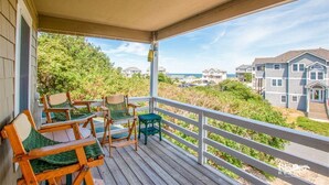 En overdækket veranda med træstole og et lille bord, med udsigt over et boligområde med huse og en strand.
