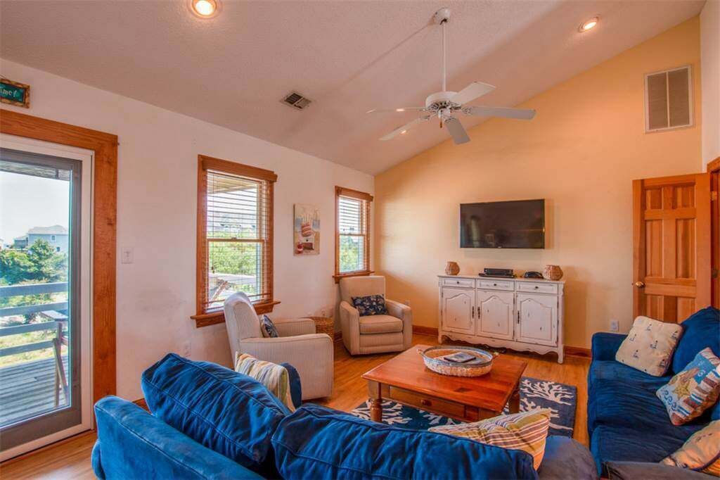 A spacious living room with a ceiling fan, a large TV, and a wooden cabinet.