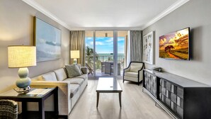 Ein modernes Hotelzimmer mit Balkon, einer Couch, einem Couchtisch, einem Fernseher und einem Schrank.