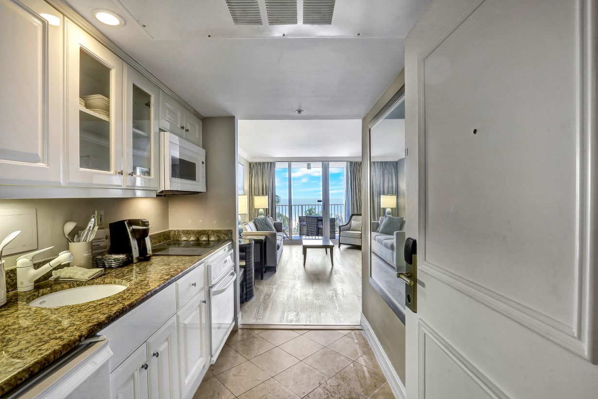 Una cocina moderna con encimera de granito, muebles blancos y vistas a un balcón.