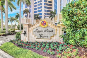 A sign for Marco Beach Ocean Resort Club Regency with a landscaped garden in front. - Lavish Beachfront Condo | Rooftop Pool/Spa/Gym (Marco Island)