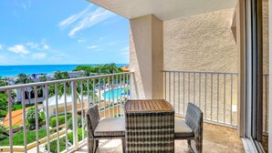 Ein Balkon mit Korbmöbeln, Blick auf Pool und Strand, und ein klarer Himmel.