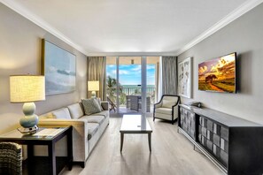A modern hotel room with a balcony, a sofa, a coffee table, a TV, and a cabinet. - Lavish Beachfront Condo | Rooftop Pool/Spa/Gym (Marco Island)