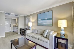 A living room with a sofa, two lamps, a coffee table, and a painting on the wall. - Lavish Beachfront Condo | Rooftop Pool/Spa/Gym (Marco Island)