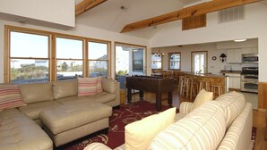 A spacious living area with a sofa, a foosball table, and a kitchen with a bar. - 2060 - DoodleBug - Corolla Retreat | Private Pool & Walk to Beach (Corolla)